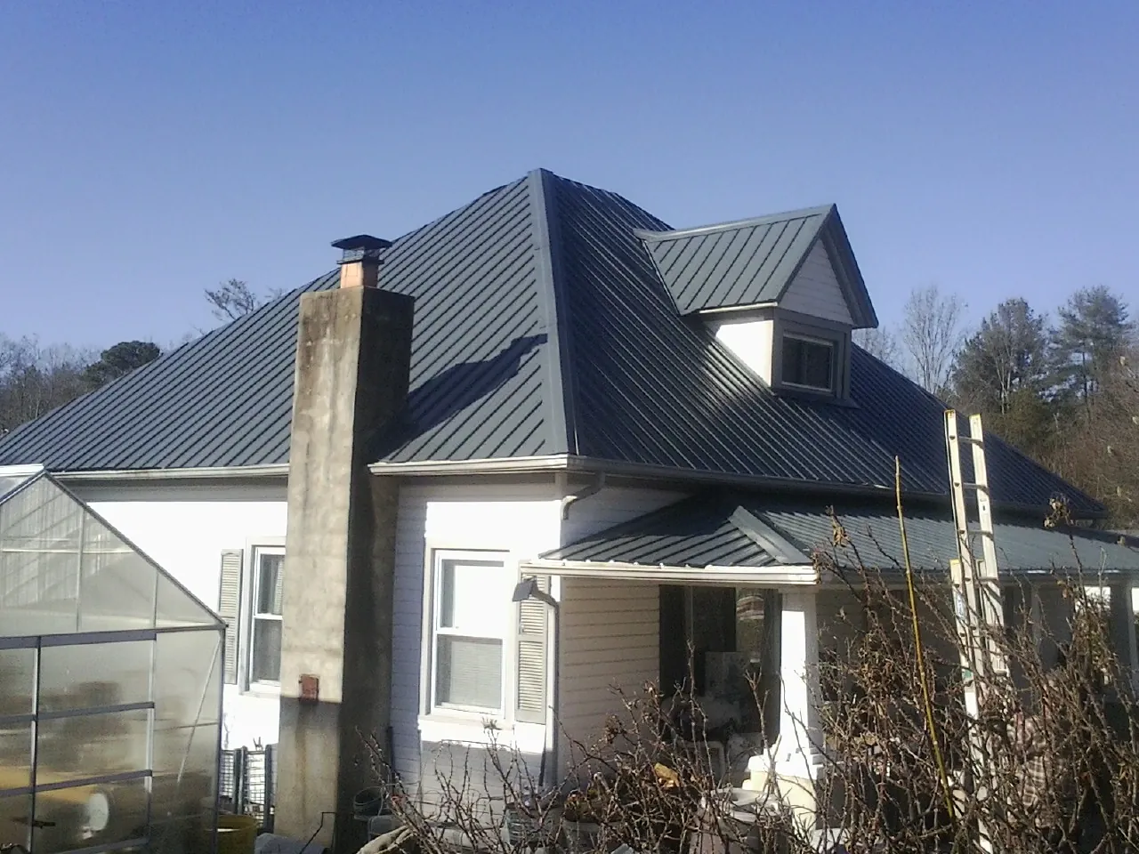 Dark blue standing seam metal roof on a white farmhouse with dormer — Slate & Tile Roof Repair by Roofing Brothers in Palmer Lake