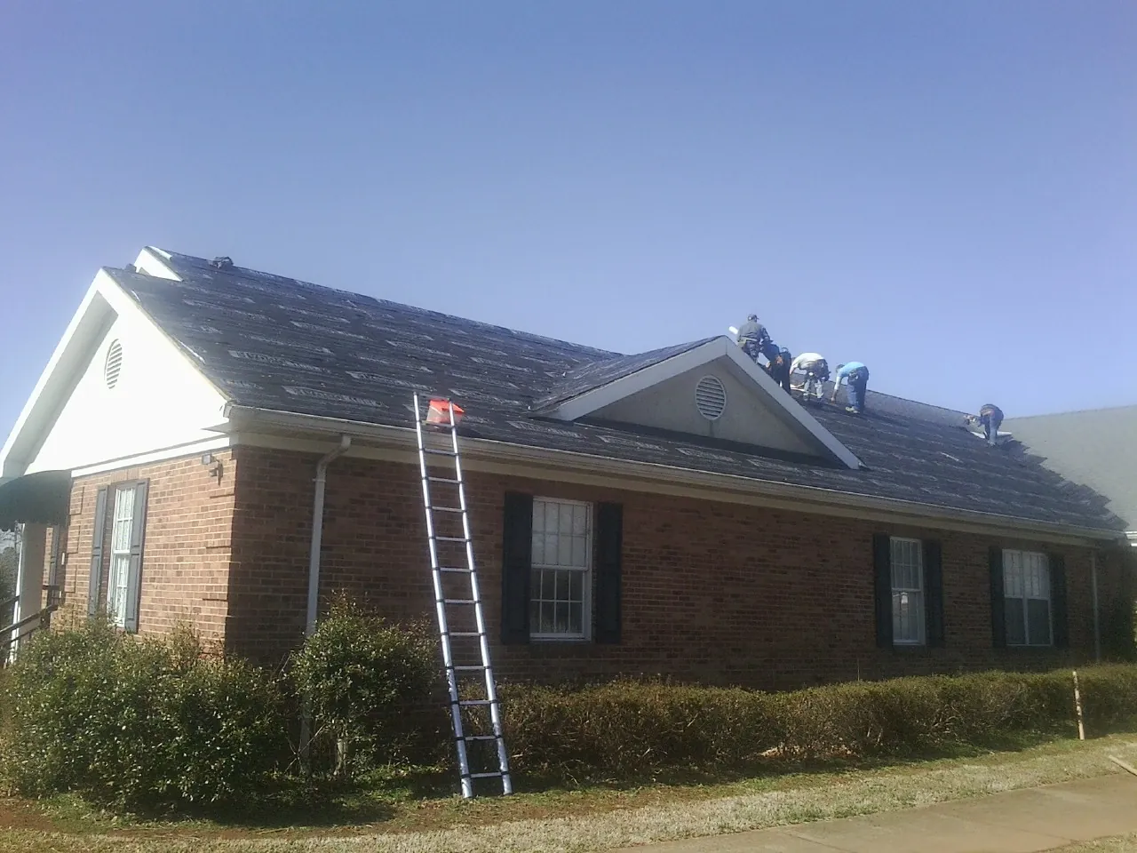 Crew tearing shingles off a brick ranch roof with a ladder set — Emergency Roof Repair work by our crew in Palmer Lake