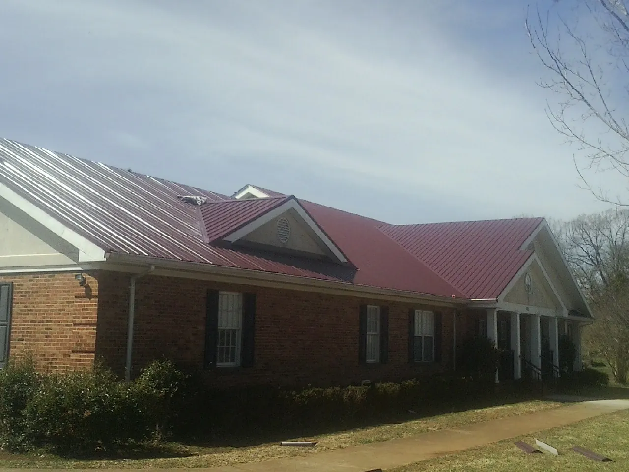 Red metal roof with gabled entries on a long brick building, from a Hail Damage Roof Repair job in Palmer Lake