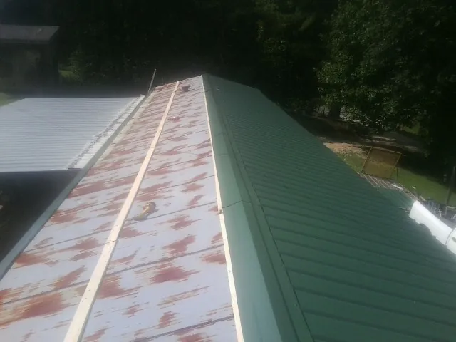 Old rusted panels beside newly installed green metal roofing — Wind Damage Roof Repair by Roofing Brothers in Palmer Lake