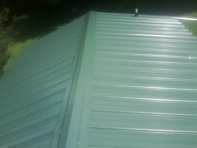New green metal panels meeting at the ridge of a roof — Flat Roof Repair work by our crew in Palmer Lake