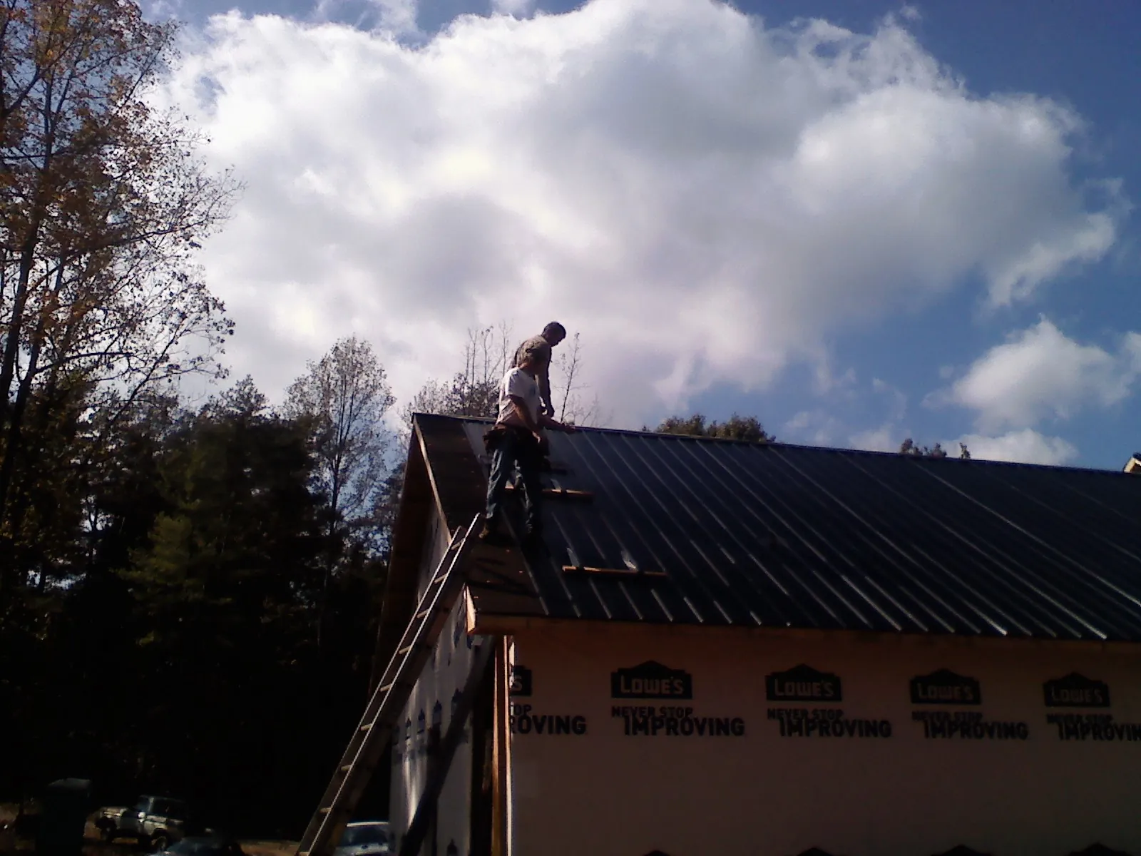 Roofer fastening dark metal panels high against a cloudy sky, from a Roof Inspection job in Palmer Lake