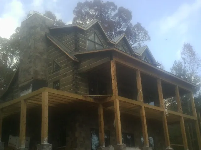 Stone chimney and dormers on a large log home with a timber porch in Palmer Lake
