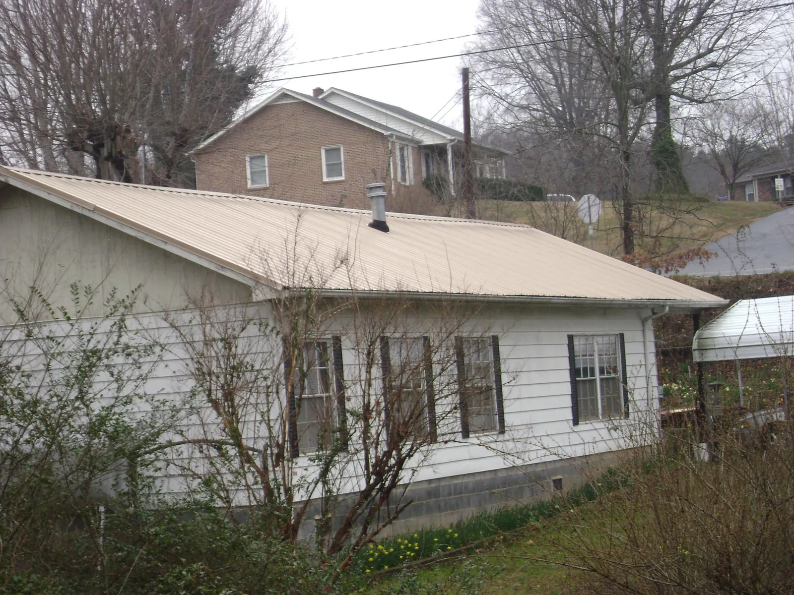 Tan metal roof on a white sided house set into a hillside — Commercial Roofing by Roofing Brothers in Palmer Lake