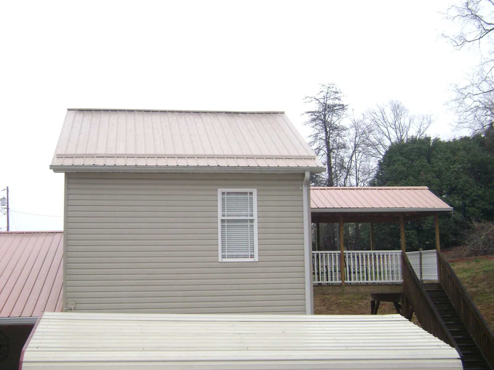 Tan metal roofs on a two story addition and attached porch, from a Roof Replacement job in Palmer Lake